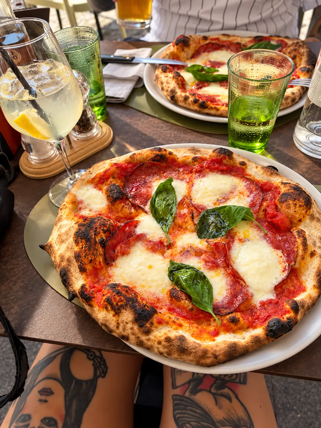 Pizza con salame piccante, mozzarella e basilico accanto a una bevanda fresca al limone, servita al tavolo